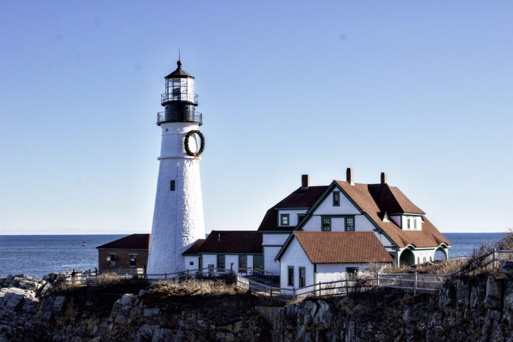 The Portland Head lighthouse on a sunny day.  The lighthouse has a very large wreath on it.
