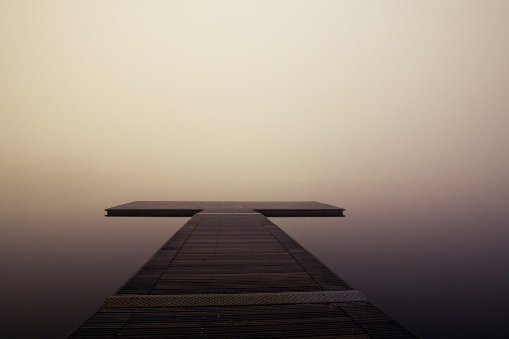 A lonely pier surrounded by water completely obscured by fog.